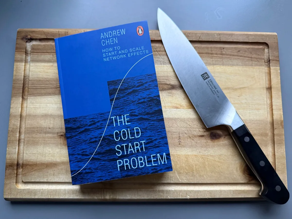 „The Cold Start Problem“ von Andrew Chen liegt auf einem hölzernen Schneidebrett neben einem Küchenmesser